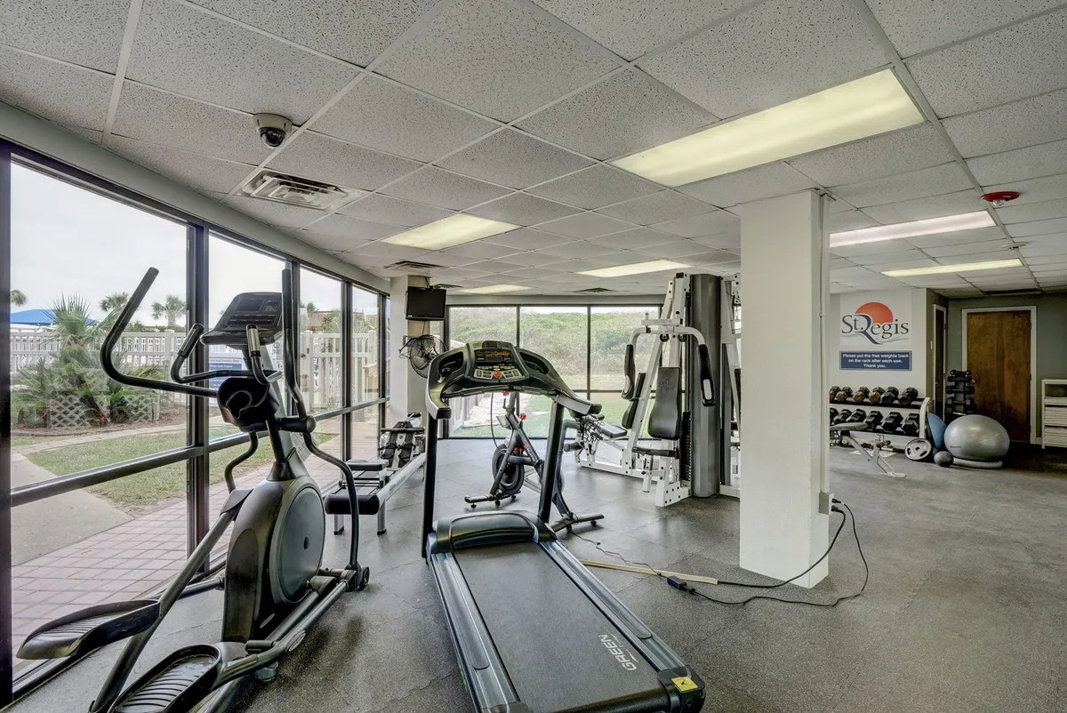 A well-equipped fitness center with treadmills, elliptical machines, and weight training equipment, all facing large windows that let in natural light. The space looks clean, modern, and motivational, ideal for workouts and wellness routines.