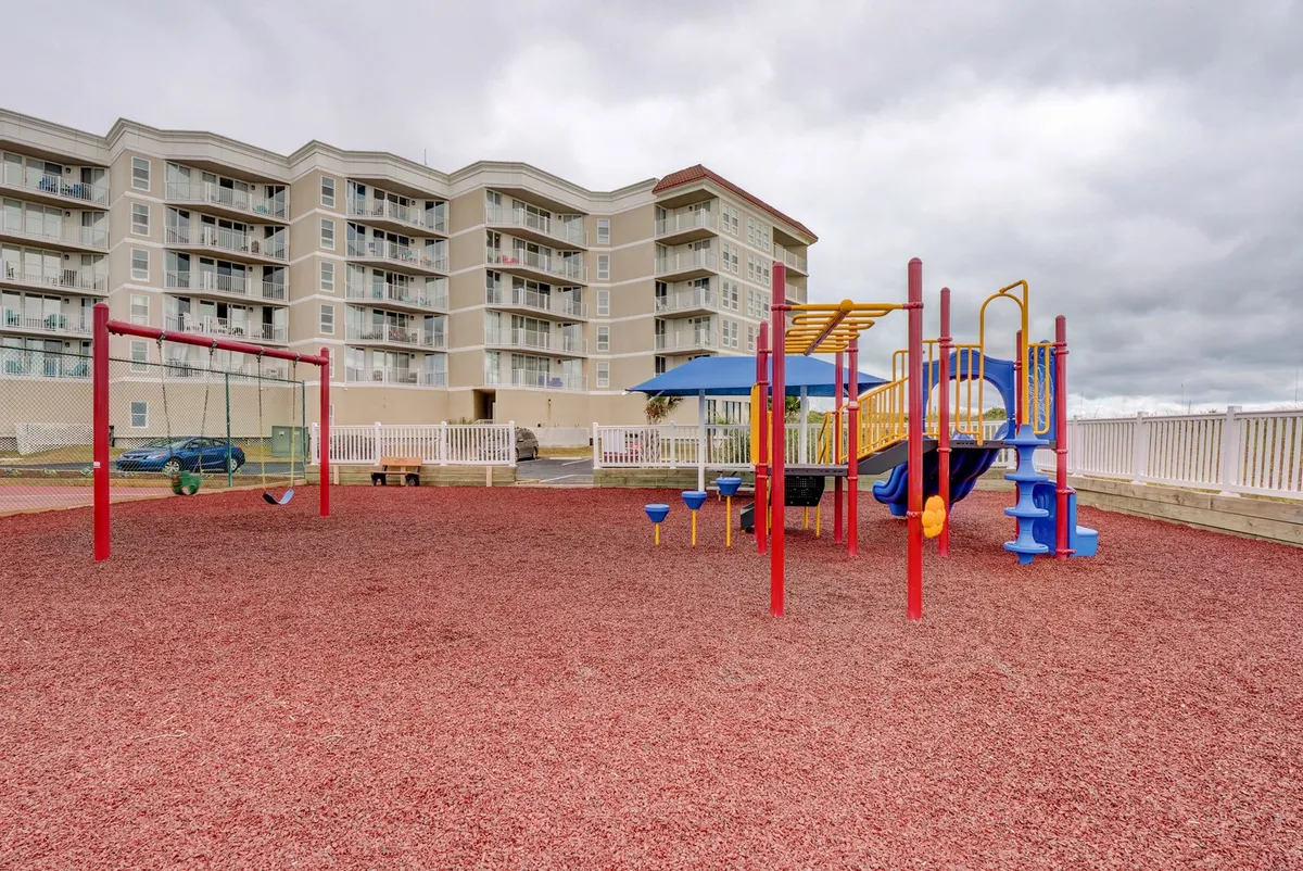 A cheerful playground scene with colorful play structures and swings, set near the apartment buildings. Children can be seen playing while families gather nearby, illustrating the communal, family-friendly environment.