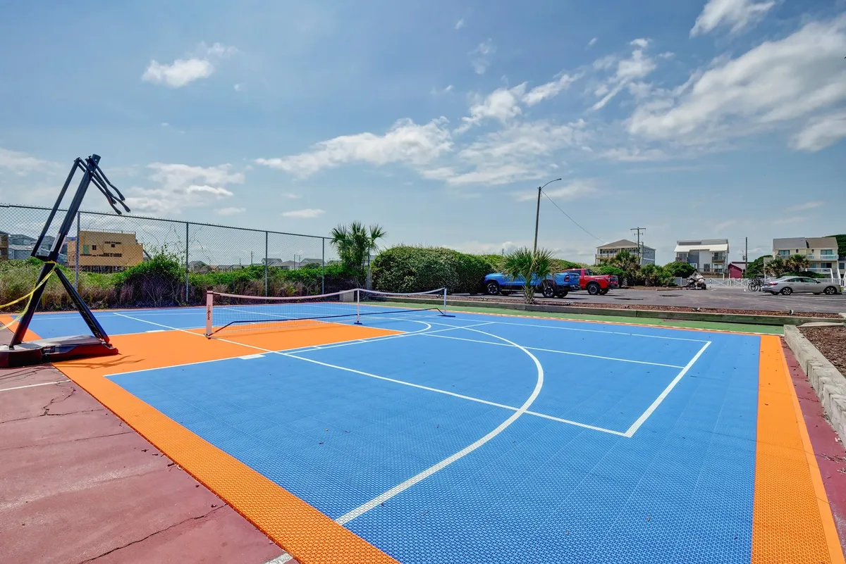 An outdoor sports court featuring a basketball hoop, tennis net, and brightly colored surface. The court is surrounded by greenery, emphasizing its active and recreational spirit. It's perfect for games, workouts, and friendly competitions.
