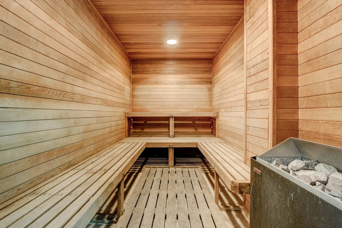 A serene sauna room with warm wood paneling and a central stone heater is framed by simple wooden benches. The space is softly lit, inviting guests to relax, socialize, and enjoy wellness routines in a calming environment.