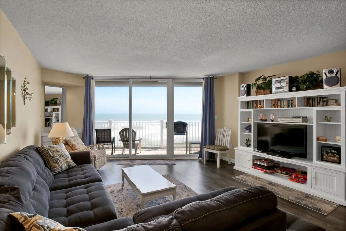 This image showcases a spacious living room with large windows offering panoramic views of the ocean. The room features a comfortable sofa and a well-appointed entertainment center, creating a welcoming environment for relaxing, socializing, or enjoying a movie night with family and friends.