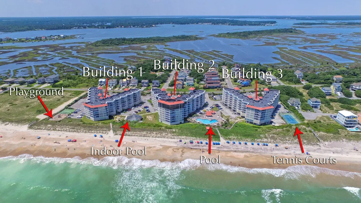 A vibrant aerial view of the St. Regis resort complex, clearly showing the outdoor pools, tennis courts, playground, and direct pathways leading to the beachfront. The image captures multiple amenities at the resort in a single frame, surrounded by the ocean and green spaces.